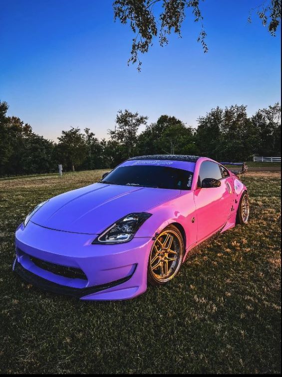 A vibrant purple-to-pink gradient sports car parked on grass under a clear blue sky.