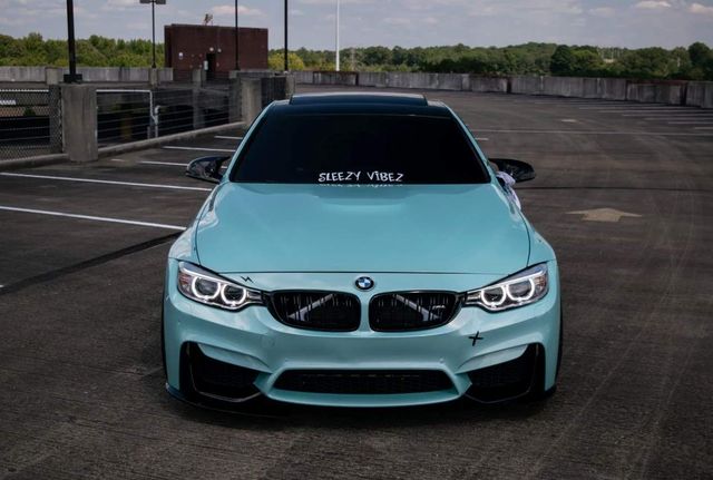 A mint green BMW sports car parked on a rooftop parking lot with 'SLEEZY VIBEZ' written on the windshield.