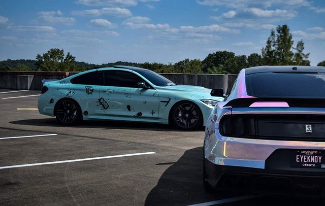 Two uniquely modified cars parked side by side under a partly cloudy sky.
