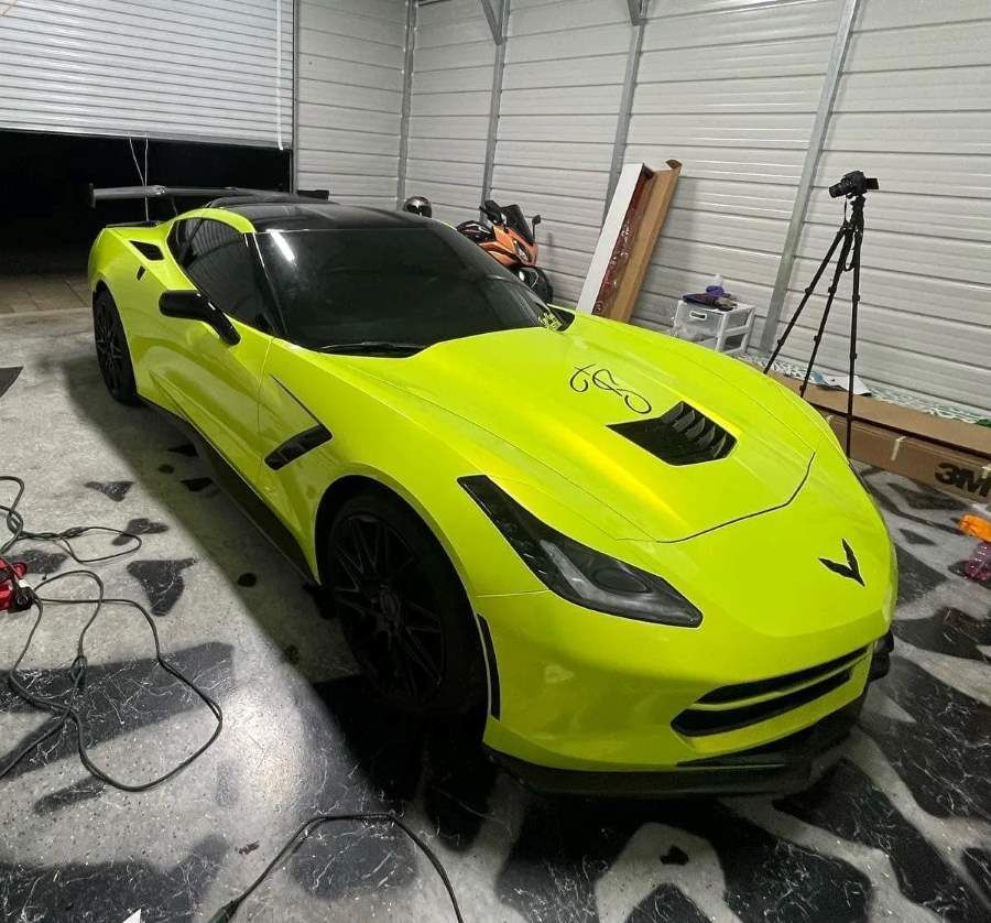 A vibrant neon yellow Chevrolet Corvette is parked inside a garage, surrounded by tools and equipment.