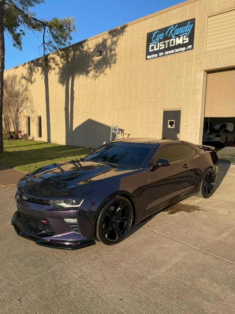 A glossy purple Chevrolet Camaro parked outside a custom car shop with a reflective finish.