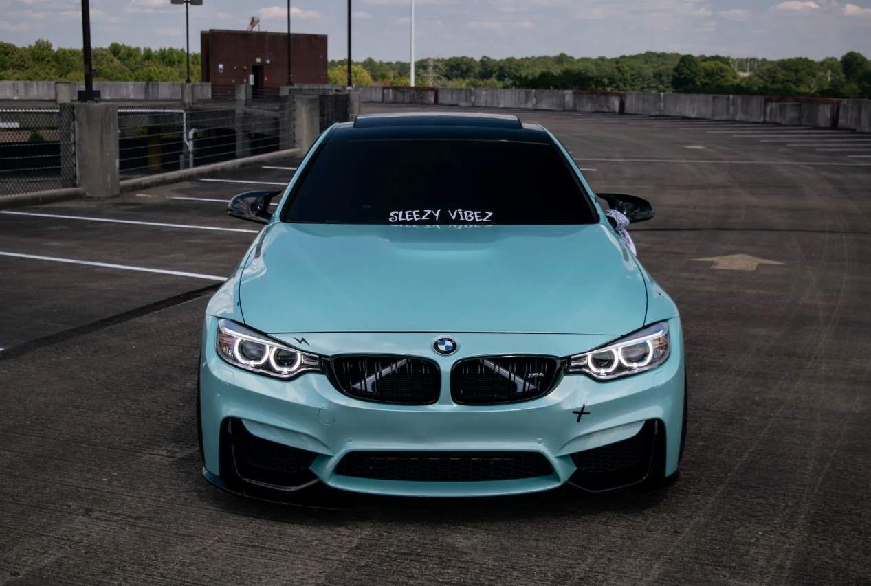 A mint green BMW M4 with custom decals parked in an empty lot.
