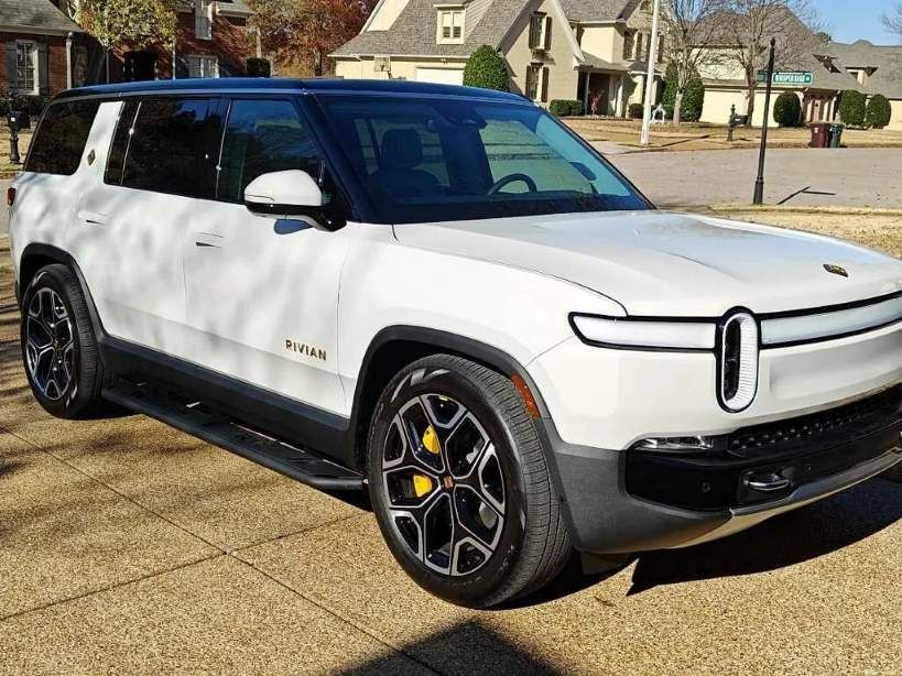 a white rivian r1s electric suv parked on a residential street.