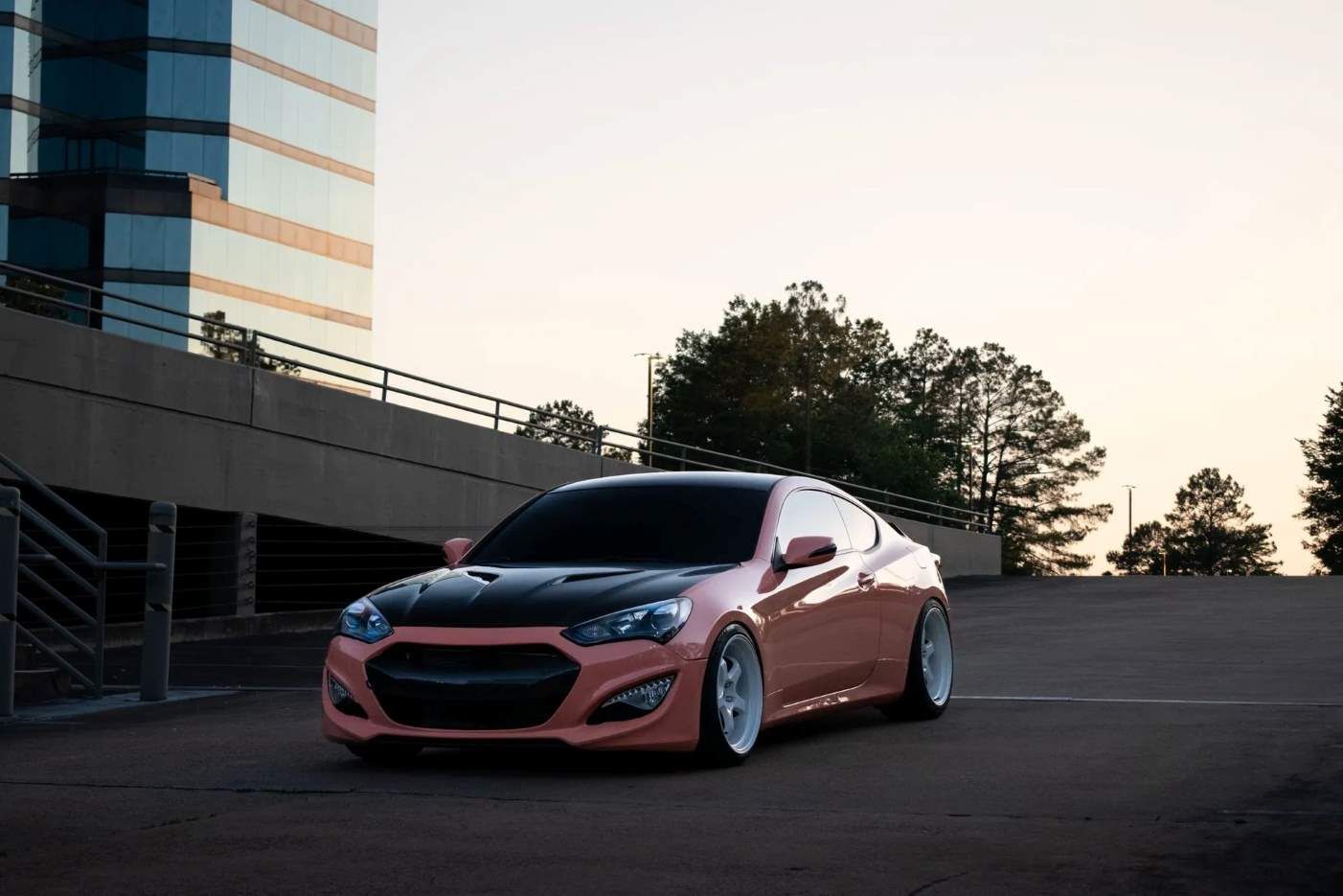 A customized pink and black coupe parked in an urban parking structure at dusk.